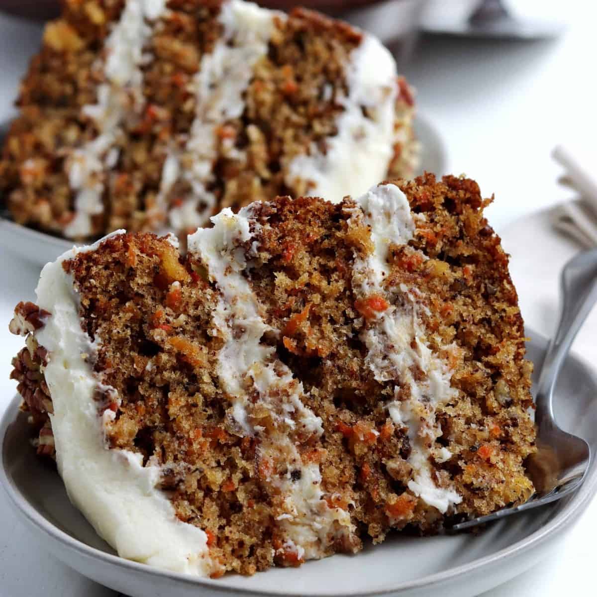 Two close up slices of cake filled with grated carrot with frosting on top.