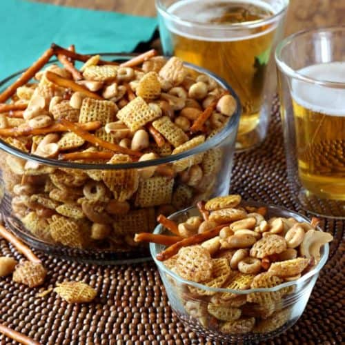 Two glass bowls filled with chex mix snack of cereal and nuts.