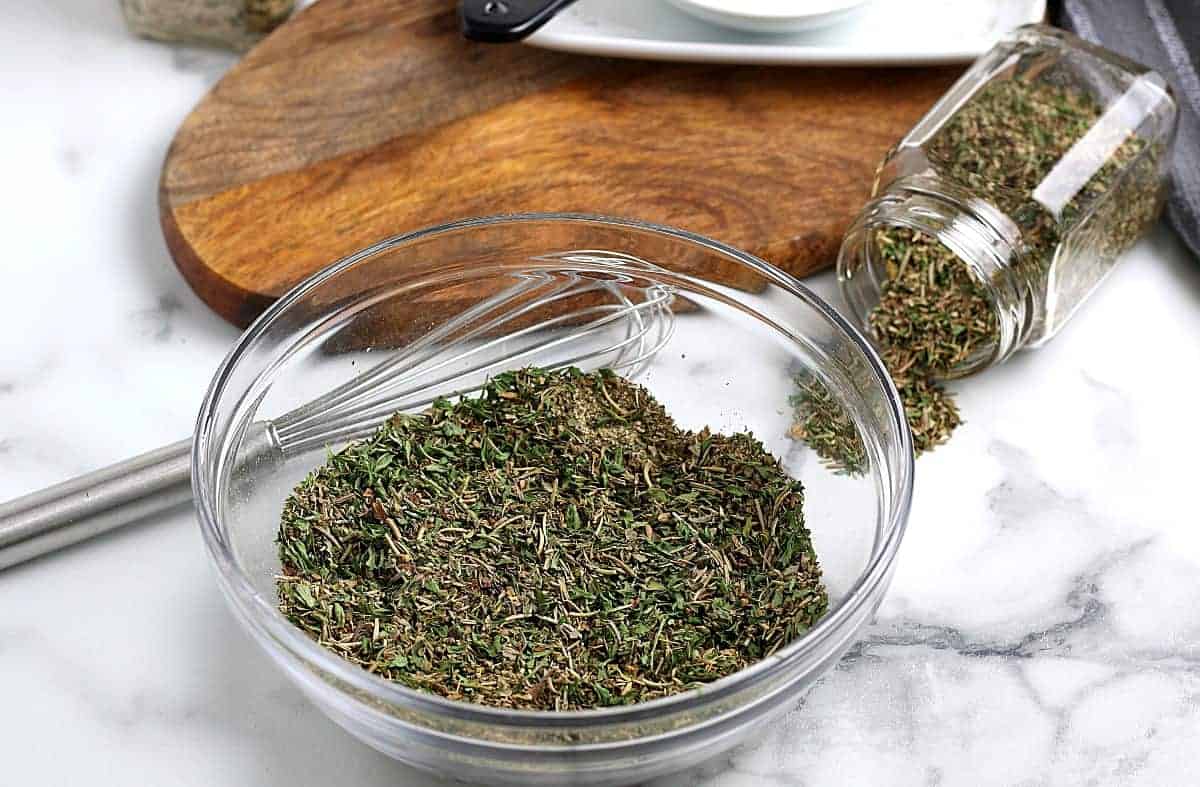 A whisk laying beside the small bowl of mixed herbs and spices.