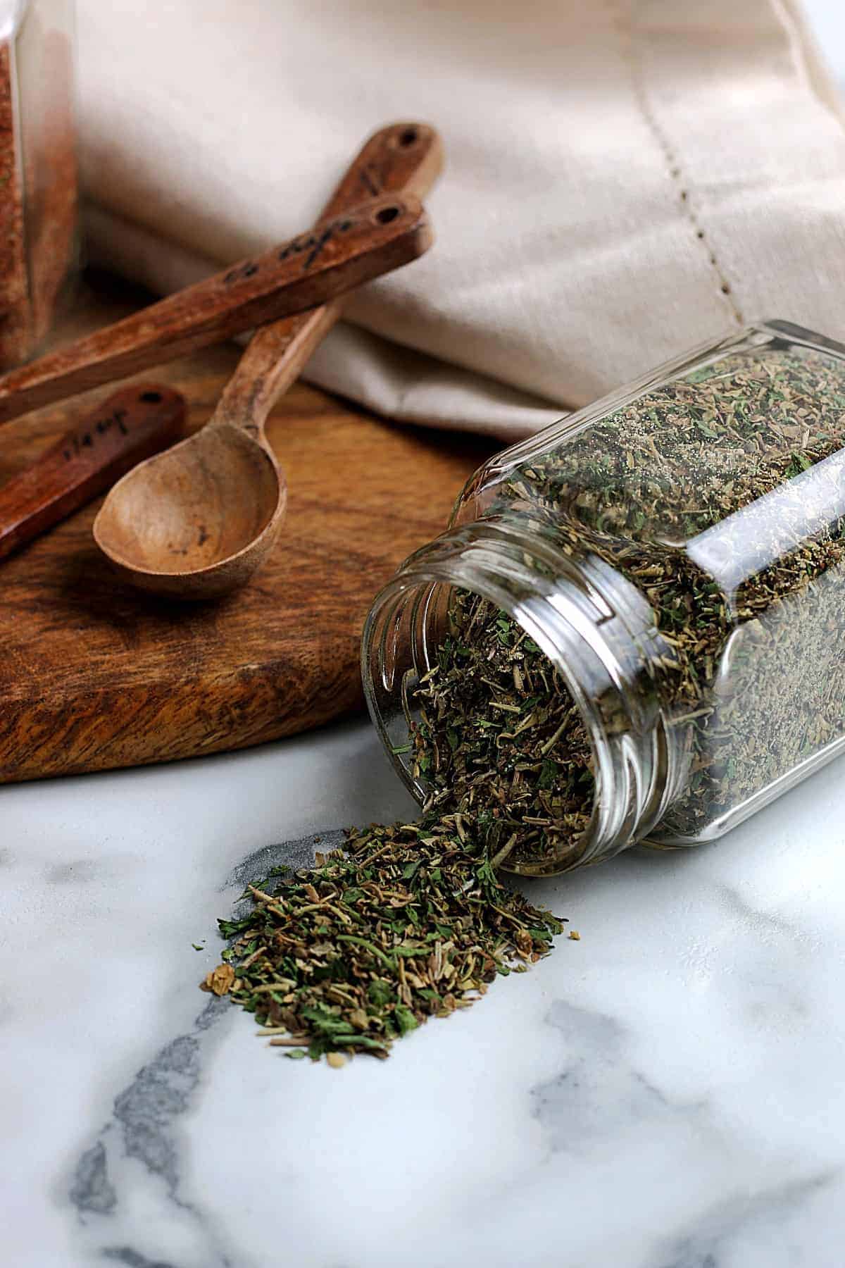 A spilled jar of Homemade Italian seasoning mix on a marble board.