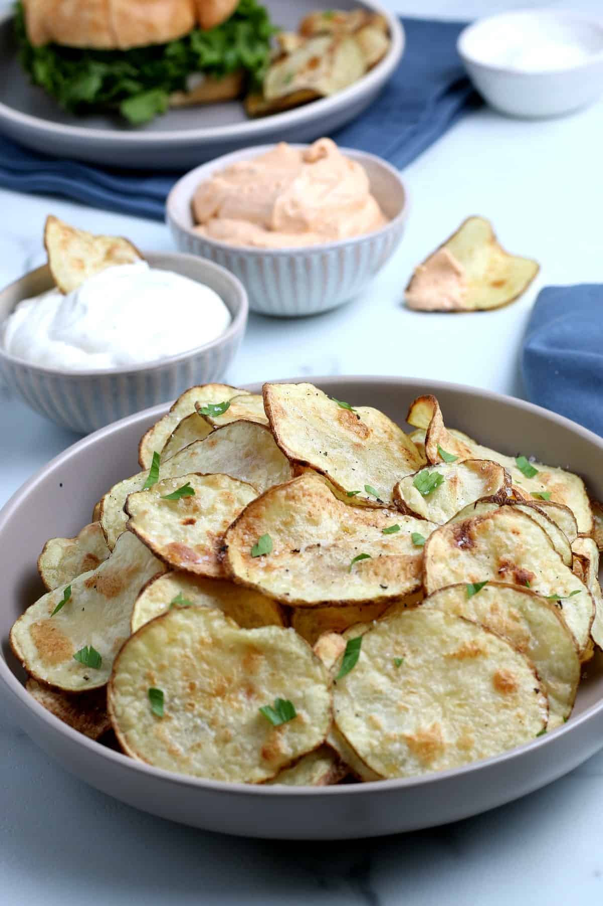 Bowl full of homemade potato chips with dipping sauces behind.