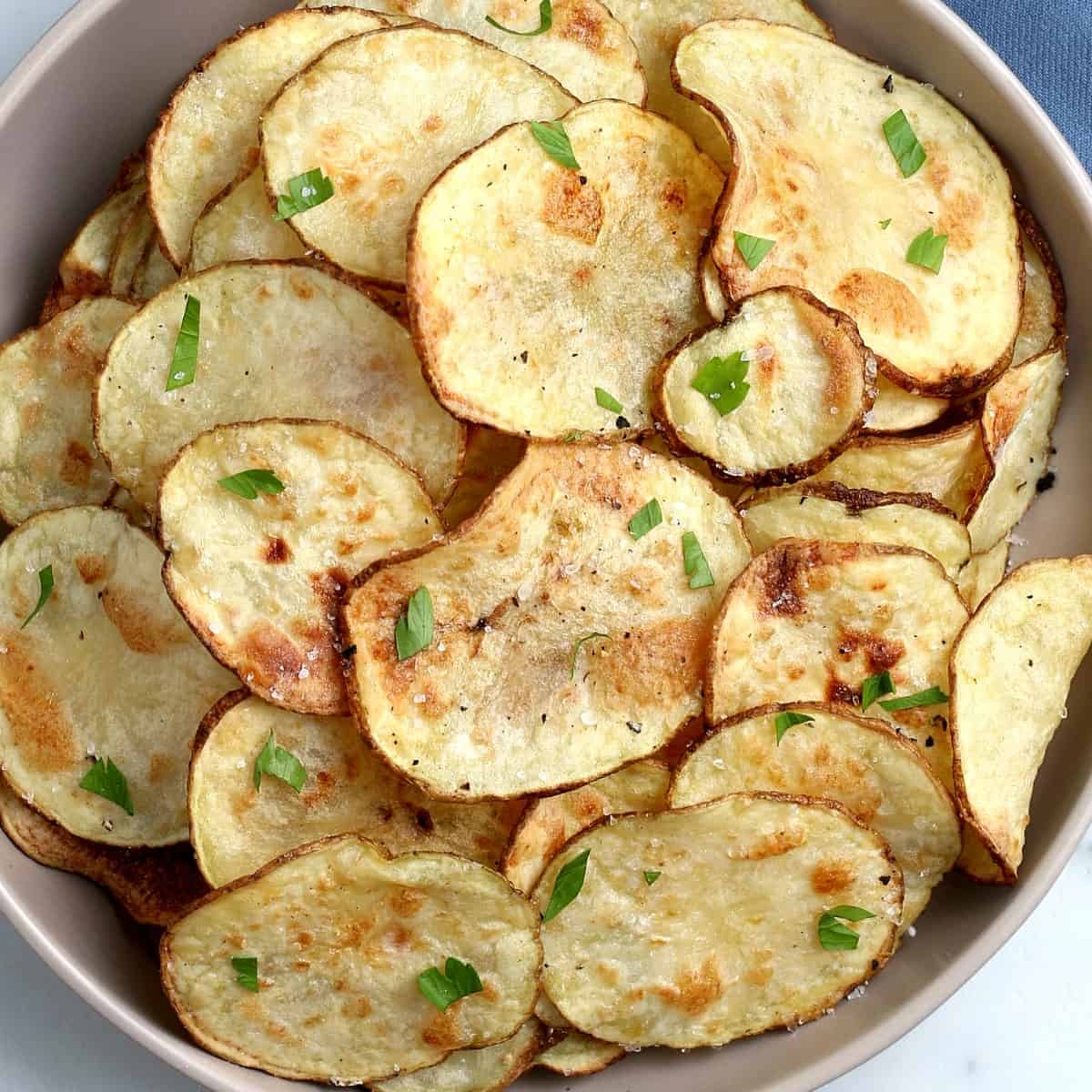 A bowl full of homemade potato chips with their skins on.