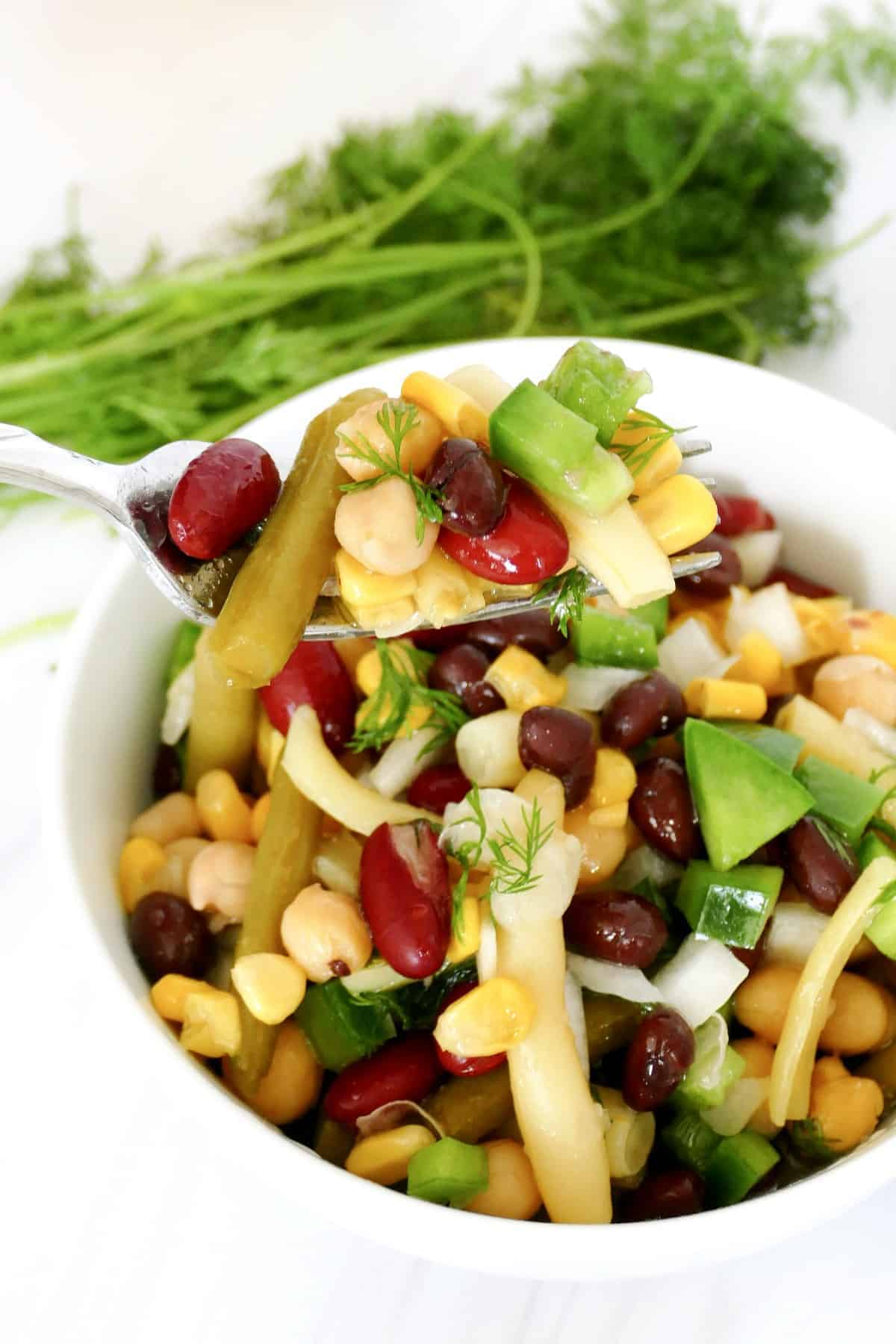 A forkful of bean salad is being help close to the camera lens.