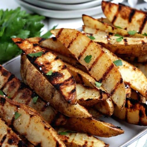 Angled stack of grilled potato wedges on a rectangular plate.