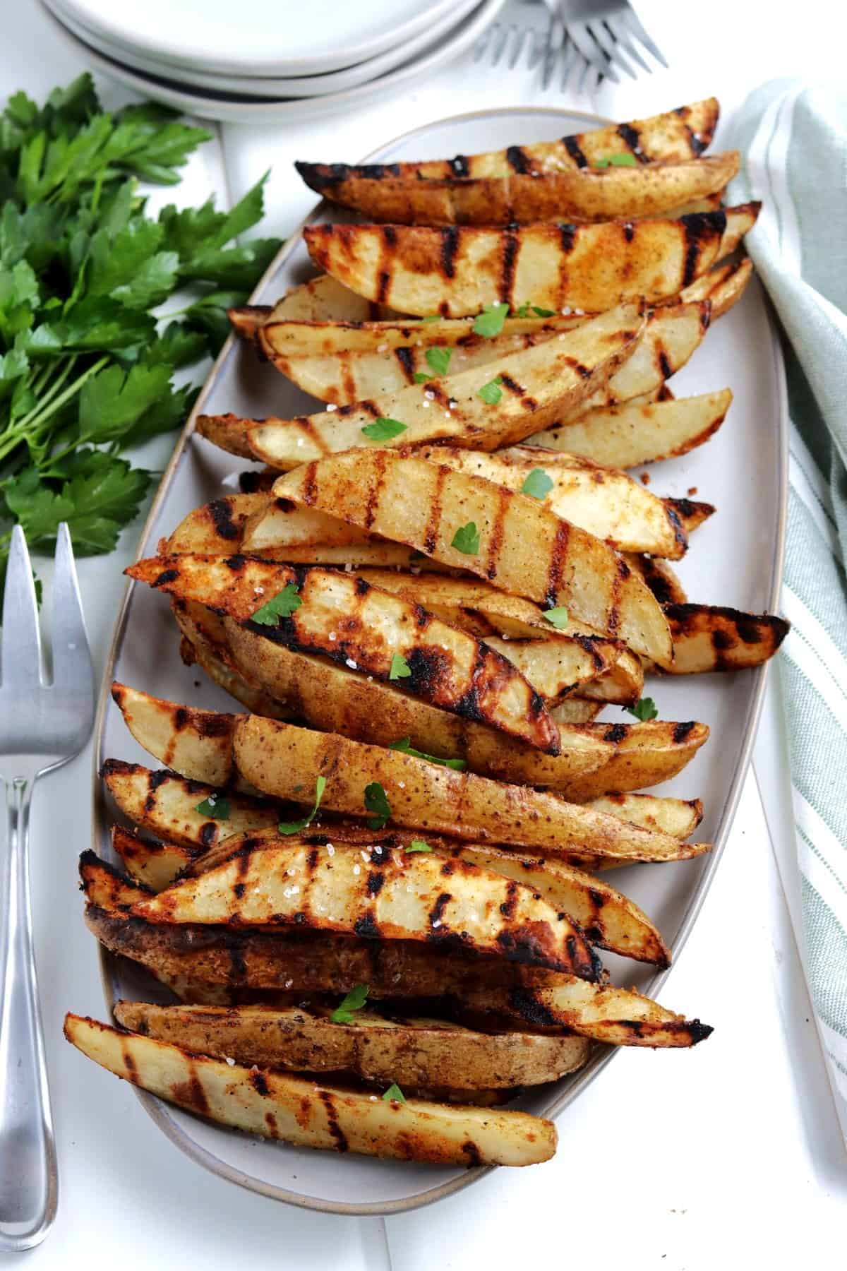 Angled pile of grilled potato wedges on an oval platter.