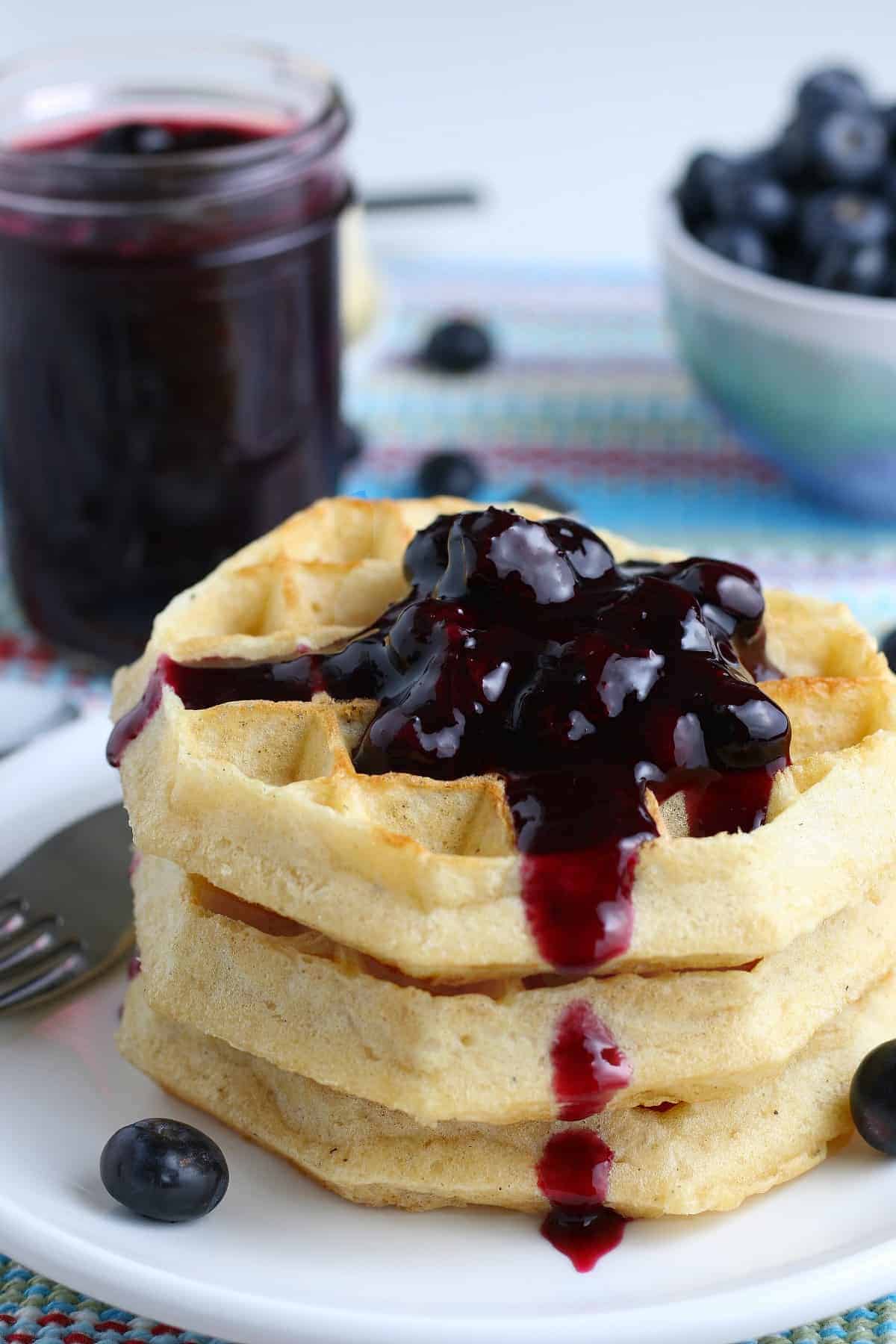 Three waffles topped with fruit topping and a jar full behind.
