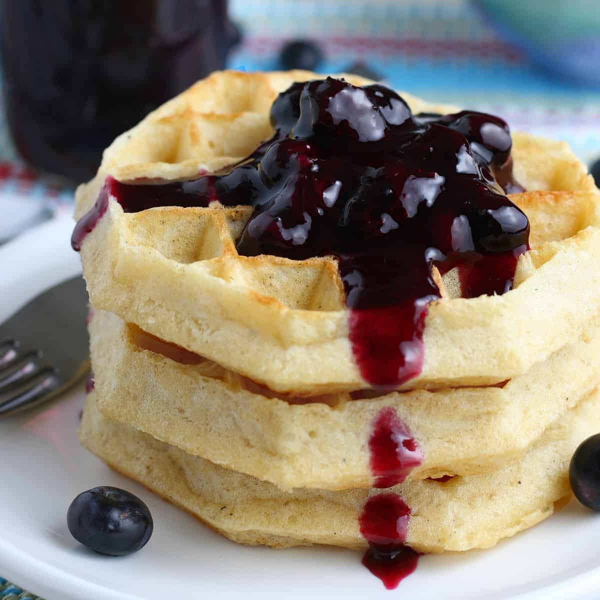 Close up of a stack of three waffles with blueberry sauce.