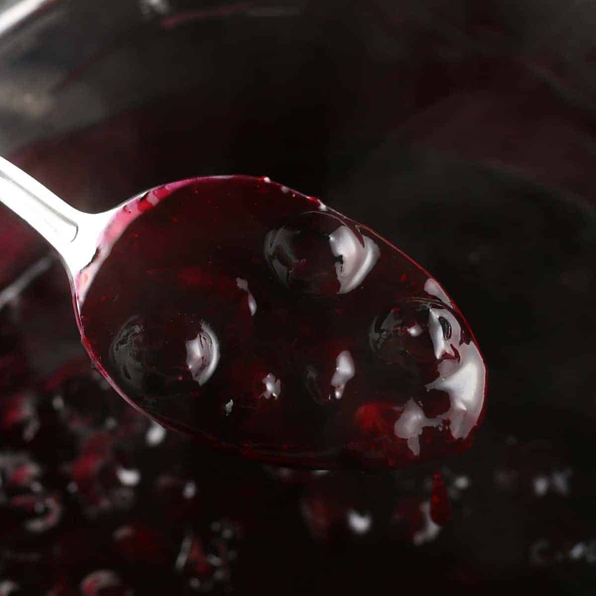 Spoonful of cooked fruit being held close to the camera.