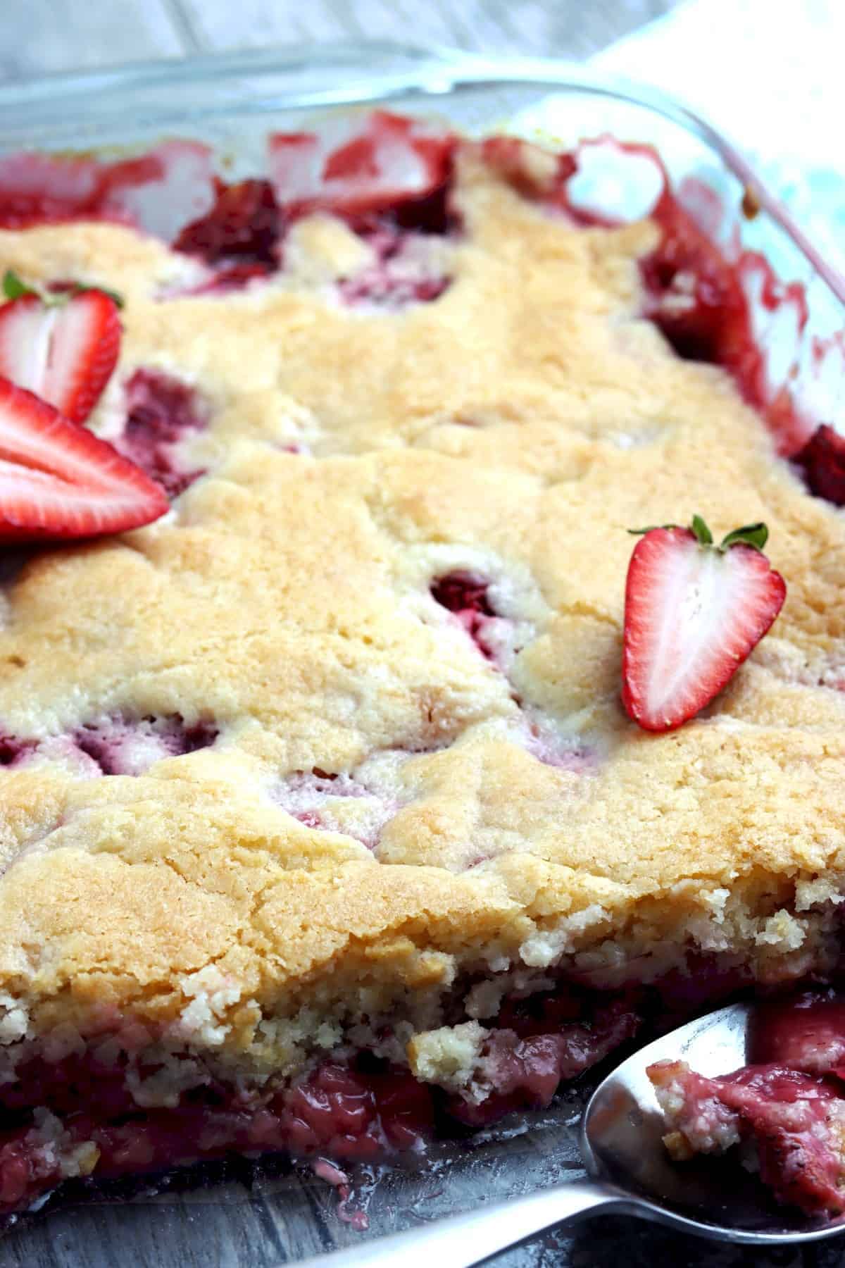 Close up of a casserole of baked strawberry cobbler with a piece cut out.