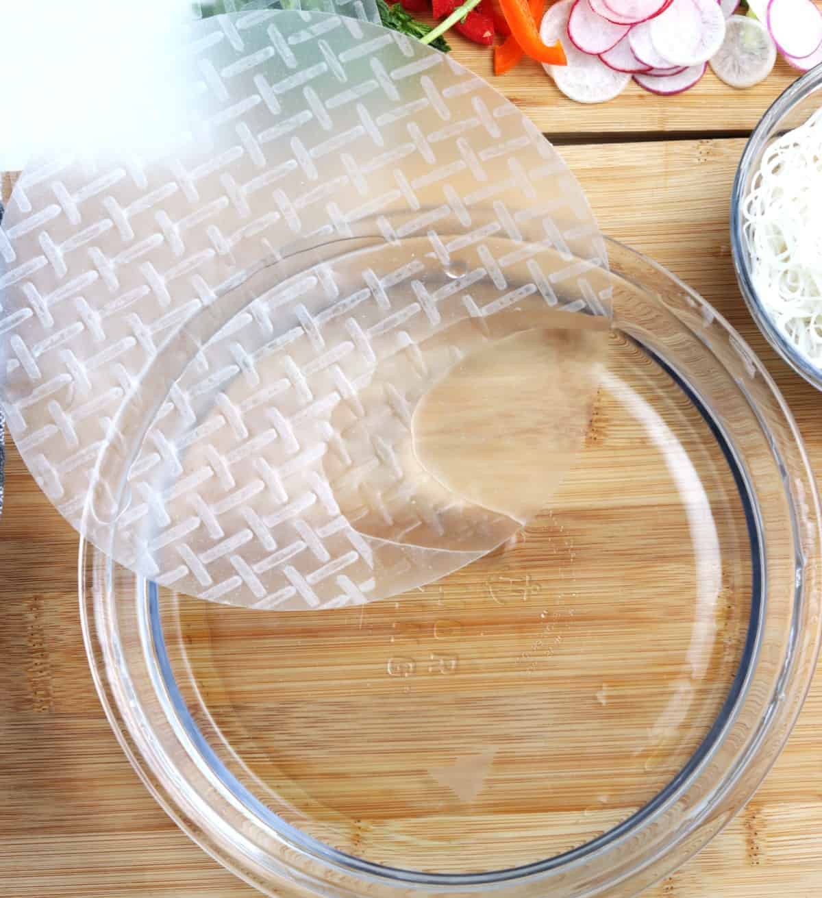 Rice paper being slid into a bowl of water for rolling.