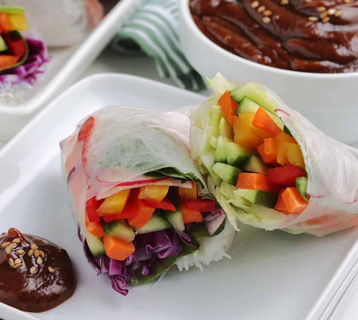 One rolled Vietnamese summer roll sliced in half with peanut dipping sauce.