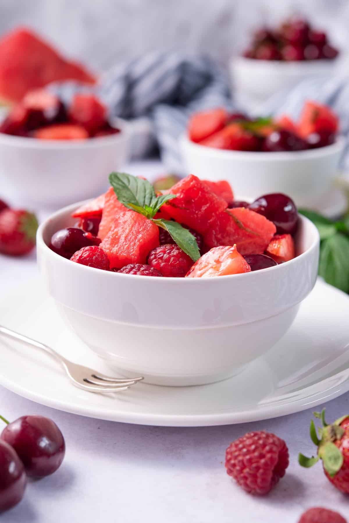 a bowl of watermelon fruit salad is garnished with fresh herbs