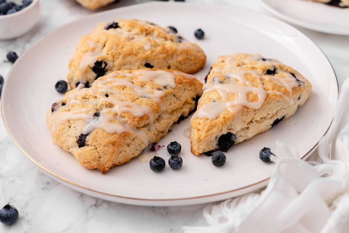 three vegan blueberry scones are served on a plate surrounded by fresh blueberries