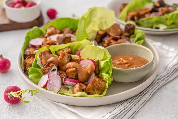 tofu lettuce wraps are served on a platter alongside a small bowl of extra peanut sauce