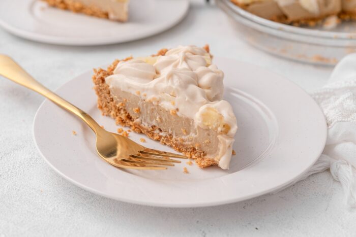 a slice of vegan banana cream pie features a thick crust layer topped with custard, sliced bananas, and whipped cream.