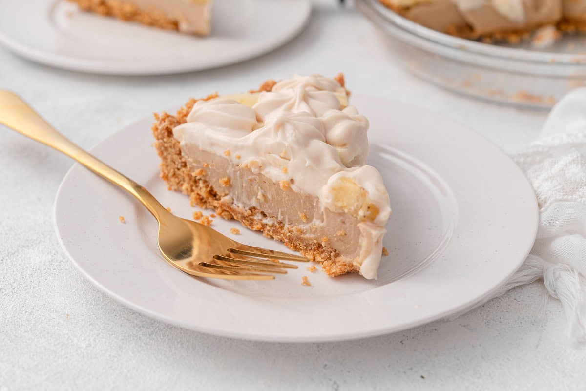 a slice of vegan banana cream pie features a thick crust layer topped with custard, sliced bananas, and whipped cream.