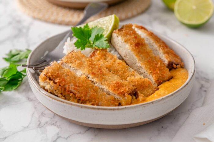 a tofu katsu cutlet is sliced into strips and garnished with lime wedges and fresh herbs